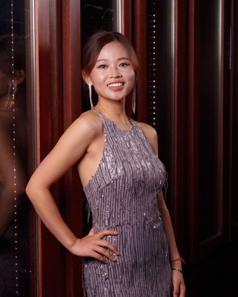 Jaya Lee in a lilac sequin dress, smiling, against dark mahogany doors