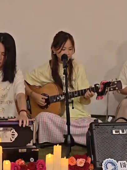 Hands on a harmonium beside a guitar, candles and rose petals