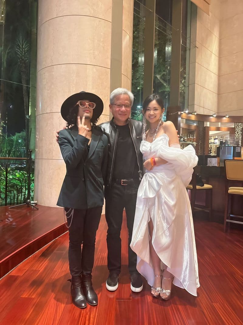 Jaya Lee in a white gown standing beside Jensen Huang in a hotel lobby